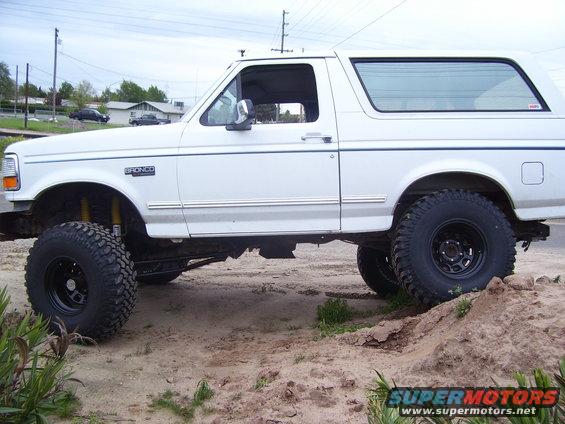 White 1994 Ford Bronco with lifted suspension and large tires, side view
