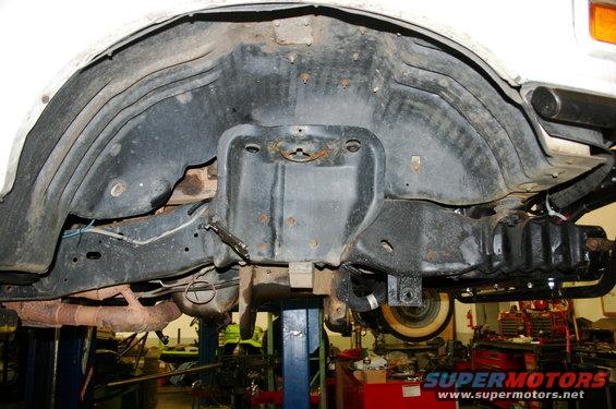 Underside of a vehicle showing the wheel well and suspension parts. A Supermotors logo is visible at the bottom right