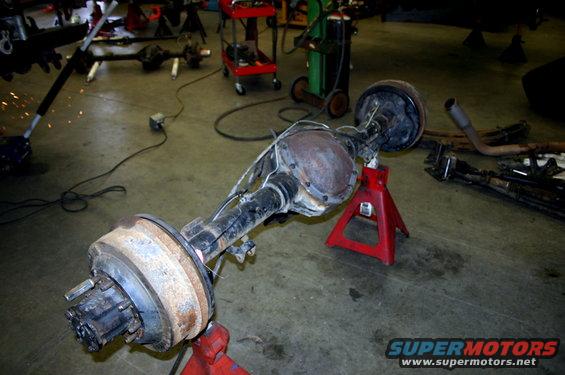 Rear axle assembly on red jack stands, with welding sparks in background