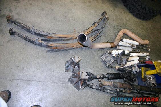Leaf springs, shocks, and exhaust pipe laid out on concrete floor