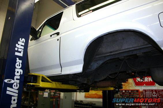 White SUV on lift, side view showing undercarriage and rear wheel well