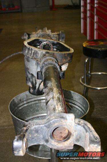 Disassembled front axle differential housing with bearing visible inside. Part is resting over a metal bucket