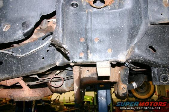 Underside view of rusty vehicle frame with suspension parts and exhaust pipe