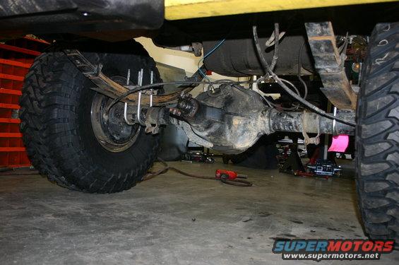 Rear axle assembly with leaf springs and U-bolts on a yellow vehicle, viewed from below