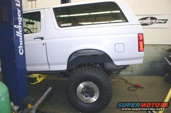 White SUV with large tires on a lift in a garage. A "Challenger Lift" sign is on the left