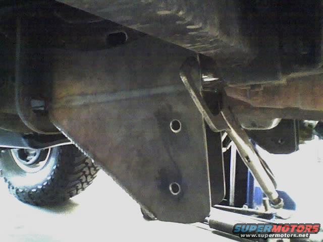 close-up of a heavy metal bracket attached to a vehicle's undercarriage, with a tire visible on the left