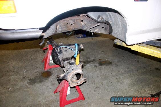 White vehicle's front suspension assembly on red jack stands, with frame visible above