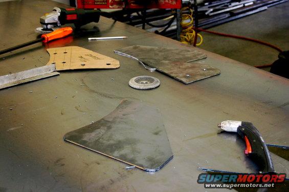 Metal pieces cut to shape, template, angle grinder, and plasma cutter on a workbench