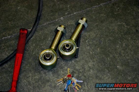 Two gold-colored suspension links with nuts, a red-handled hammer, and a set of keys on a concrete floor