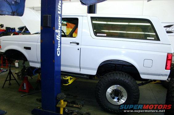 White SUV on a lift with hood up, undergoing repairs. Lift is blue with 'Challenger Lifts' text