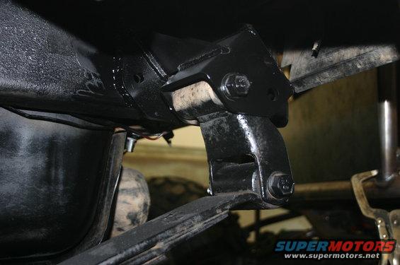 Close-up of a black metal bracket attached to a vehicle frame, with a leaf spring visible below