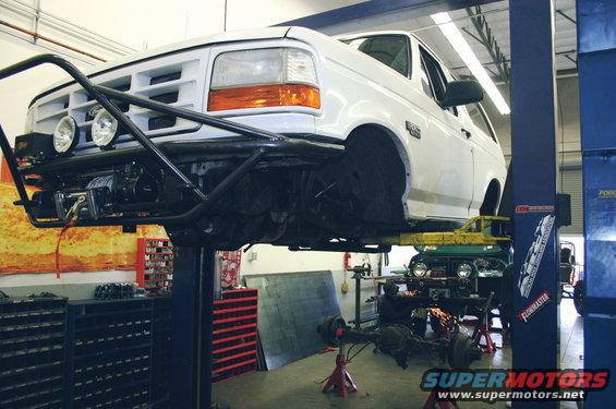 White SUV on a lift with a custom bumper and winch. Another vehicle is visible underneath