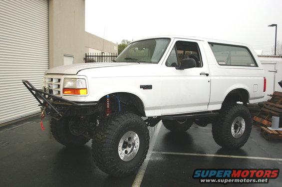 White Ford Bronco with aftermarket bumper and large tires parked outside a garage