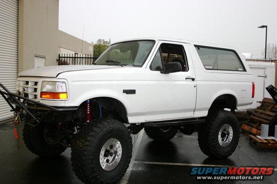 White 1992 Ford Bronco with large tires and custom bumper, parked outside