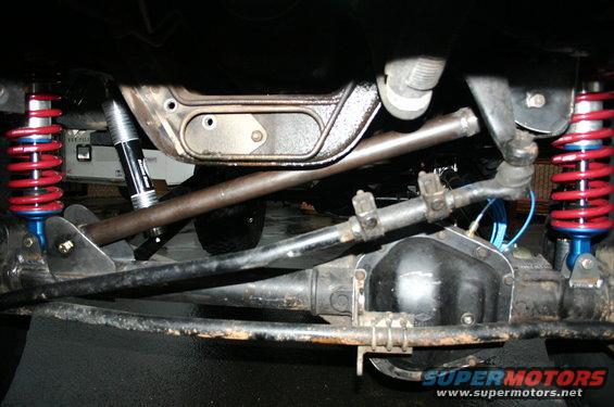 Close-up of modified front suspension with red coilover shocks, steering linkage, and differential housing