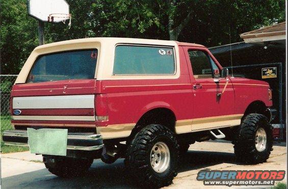 Red and tan Ford Bronco with lifted suspension and large tires, viewed from the rear three-quarter angle