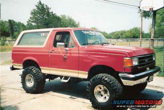 Red 1990 Ford Bronco with lifted suspension and white top
