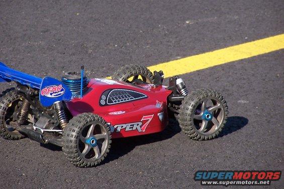 Red remote control buggy with blue wing and "HYPER 7" graphics on asphalt with yellow line