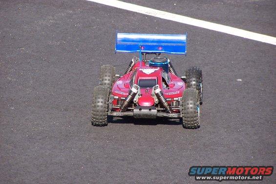 Red remote control buggy with a blue spoiler on a paved surface
