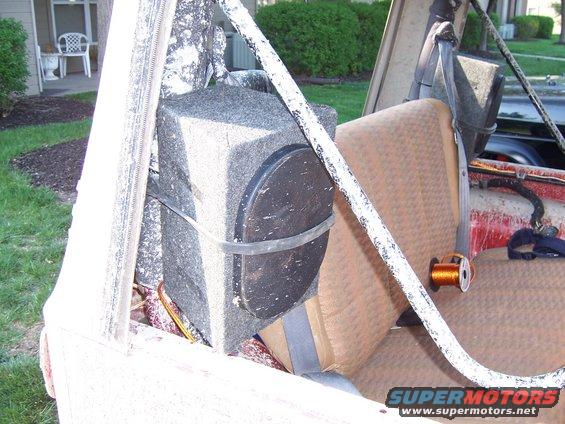 Interior of a vehicle showing a large speaker mounted behind the passenger seat, with tan upholstery and white roll bar