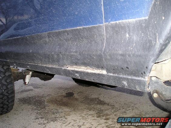 Close-up of a blue vehicle's lower body side, showing the black trim and part of a tire