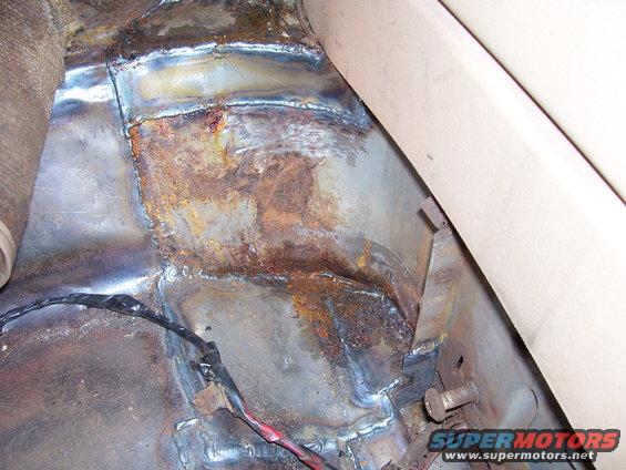 Rusted floor pan with visible welding repairs and wiring, interior view