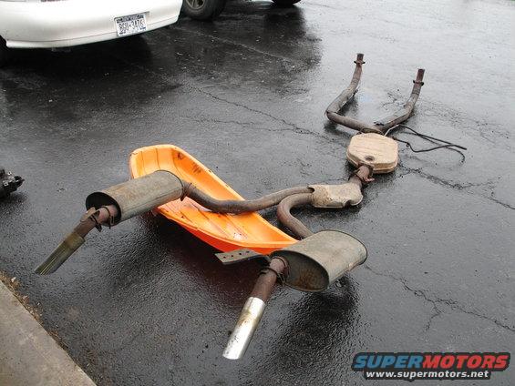 Exhaust system on an orange snow sled, with a white car in the background