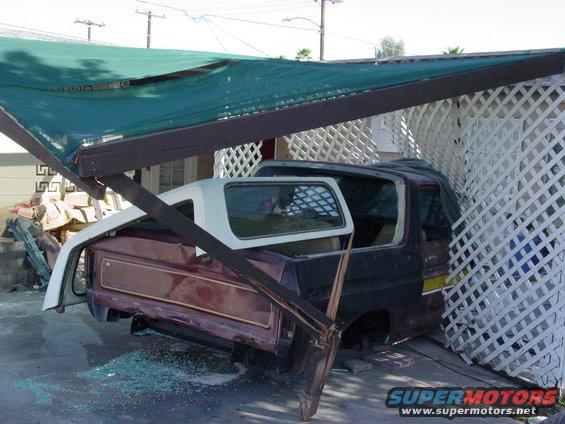 Maroon Ford Bronco body with white removable top, missing windows, parked under a green awning