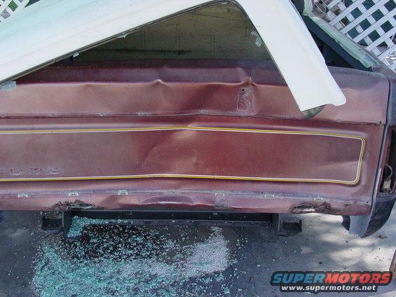 Maroon rear quarter panel with gold trim, showing significant rear-end damage and shattered glass on the ground