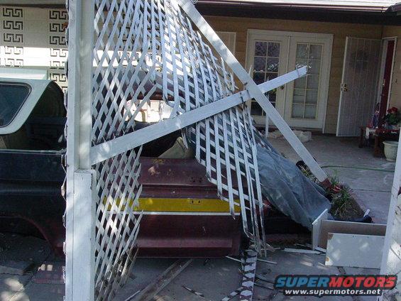 part of a dark pickup truck bed with a maroon and yellow stripe, next to a broken white lattice structure