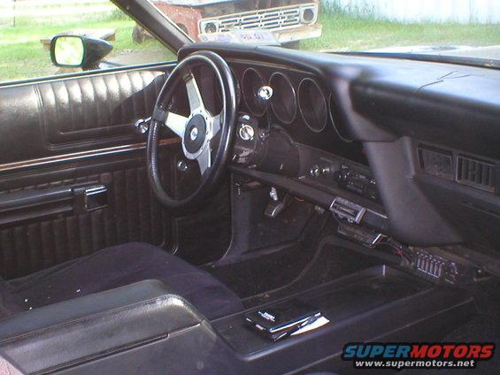 Interior of a 1972 Ford Ranchero, showing the dashboard, steering wheel, and driver's seat. A second vehicle is visible through the windshield