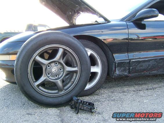 Black 1996 Ford Probe GT with hood open, spare tire in front, and damaged rocker panel