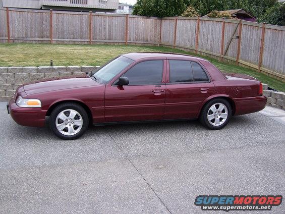 Maroon 2005 Ford Crown Victoria parked on a concrete driveway with a wooden fence and lawn in the background