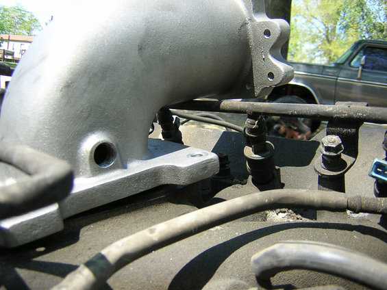 Close-up of a silver intake manifold part with hoses and bolts visible