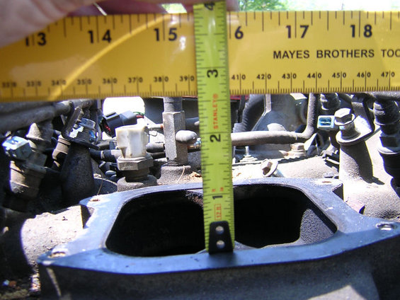 Measuring the opening of an engine intake manifold with a tape measure. The manifold has several sensors and hoses attached