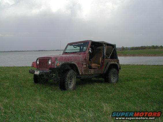 Red Jeep Wrangler parked on grass near a body of water, soft top removed