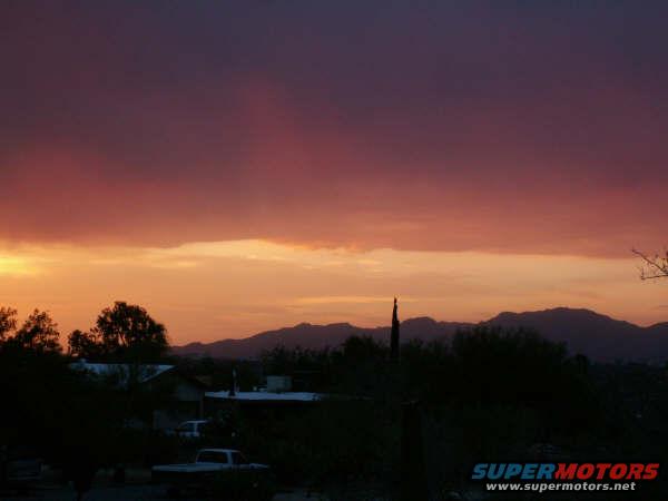White pickup truck rear view, parked in silhouette against a sunset sky with mountains and houses