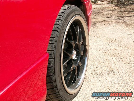 Close-up of a red car's fender and a black multi-spoke wheel with a polished lip. Tire tread is visible
