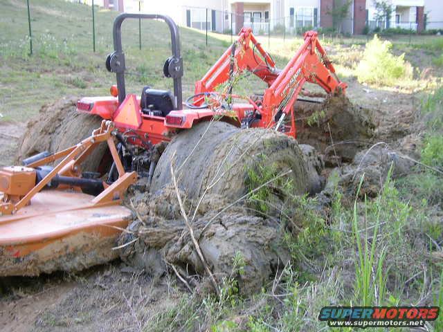 Orange tractor stuck in mud with loader arm extended
