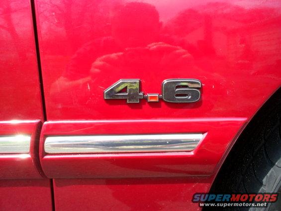 Red car's "4.6" emblem and chrome trim on door panel, with part of tire visible
