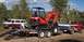 1990 Ford Bronco - A red pickup truck tows a trailer carrying a Kubota excavator, with a van visible in the background.