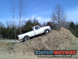 White pickup truck, likely 1992-1997 Ford F-Series, climbing a dirt mound. SuperMotors.net logo visible