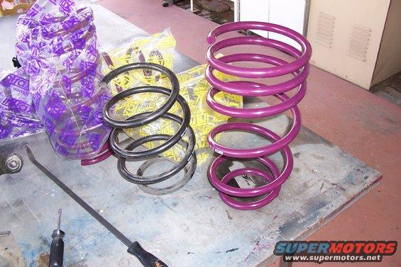 Two sets of suspension coil springs, one purple and one black, on a workbench with packaging
