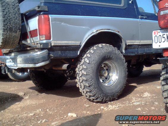 Rear quarter view of a blue and silver SUV with large off-road tires and a spare tire mounted on the back