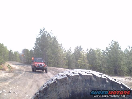 Red Jeep Wrangler on a dirt road, seen from another vehicle's tire