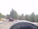 1991 Ford Bronco - A red Jeep Wrangler drives on a dirt road through a wooded area, with another vehicle's tire in the foreground.