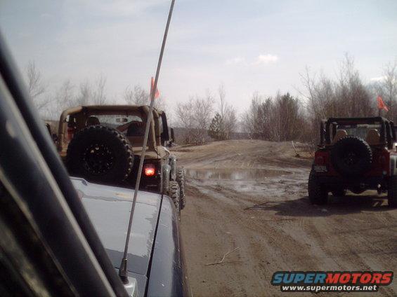 Two Jeeps driving on a muddy off-road trail with puddles