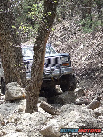 1986 Ford Bronco navigating a rocky trail, front grille and bumper visible