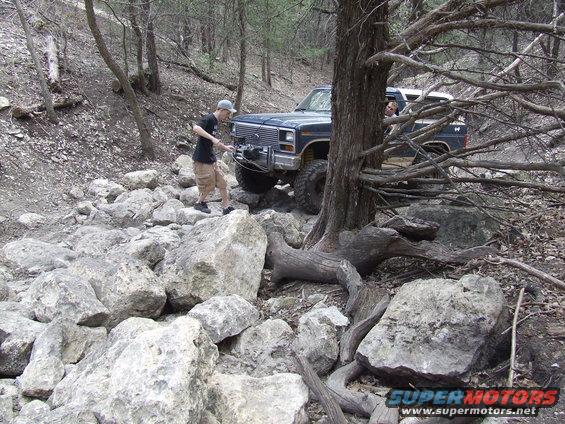 guy winching a dark blue 1980s pickup truck through rocks
