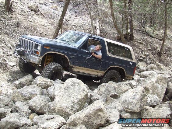 1986 Ford Bronco navigating a rocky trail with a driver visible